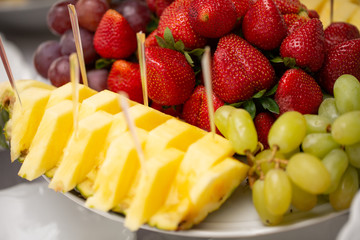 decorated various fruits on plate at restaurant, wedding catering. Pineapple, strawberry, green grape.