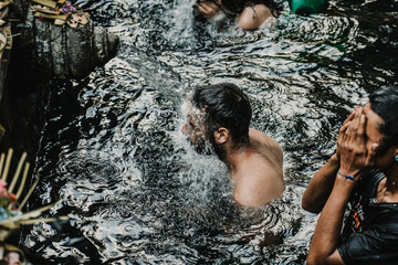 .Young tourist visiting the Pura Tirta Temple in Bali, indonesia dressed in a sarong. Doing the ritual in each of the jets of water. Spiritual visit. Travel concept..