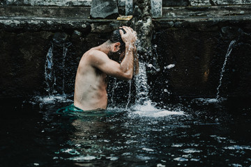 Fototapeta na wymiar .Young tourist visiting the Pura Tirta Temple in Bali, indonesia dressed in a sarong. Doing the ritual in each of the jets of water. Spiritual visit. Travel concept..