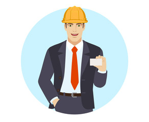 Businessman in construction helmet with hand in pocket showing the business card