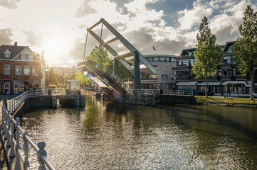 Tree-lined wide canal with houses and lifted bascule bridge on sunset in Weesp. Quiet and pleasant village full of canals and green near Amsterdam. Northern Netherlands.