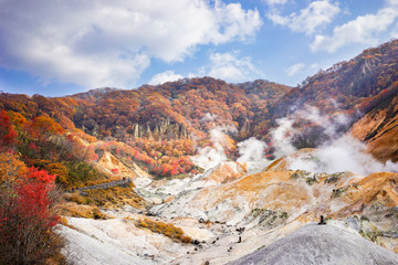 Beautiful sunny day at Noboribetsu Jigokudani or Hell Valley in Hokkaido, Japan. Autumn season, red leaves, blue sky and sulfur gas steaming out from ground.