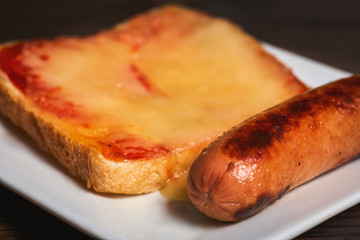 Sandwich with melted cheese and fried sausage close-up against the background of a dark tree.