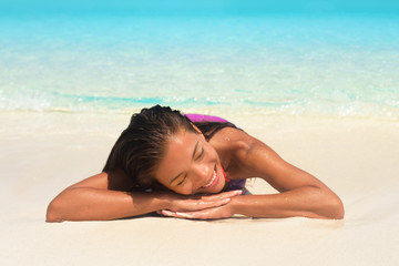 Beach summer relaxation spa retreat woman sunbathing lying down on white sand in tropical paradise. Bikini Asian girl relaxing sleeping enjoying sun getaway.