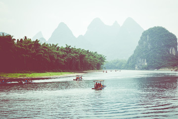 Scenic view of small tourist bamboo rafts sailing along the Li River among green woods and karst mountains at Yangshuo County of Guilin, China. Yangshuo is a popular tourist destination of Asia.