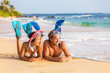 Beach couple snorkel people on summer snorkeling travel holiday watersport leisure activity. Young adults enjoying vacation relaxing lying down on sand near water after swim.