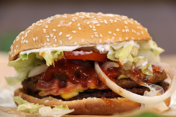 hamburger on paper with round bread and white sesame, beef and vegetable. It is a round patty of beef, fried or grilled and typically served on a bun or roll and garnished with various condiments.
