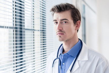 Close-up portrait of a young serious doctor looking at camera with determination and dedication in a modern hospital or medical clinic