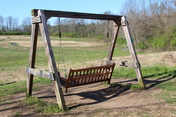 Fototapeta na wymiar The wood swinging bench overlooking the field.