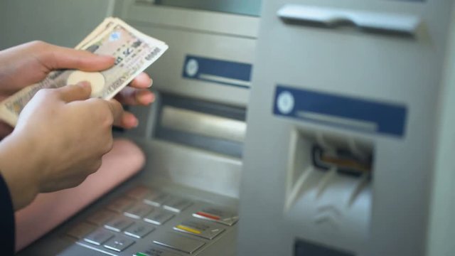 Female counting Japanese Yen withdrawn from ATM, putting cash in purse, tourism