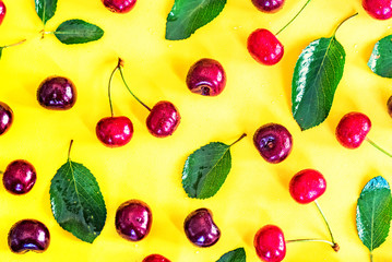 Sweet ripe cherries and leaves on yellow background