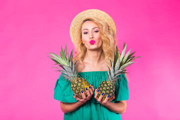 Happy young woman holding a pineapple on a pink background. Summer, diet and holidays concept