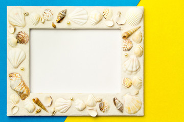 Naklejka na ściany i meble Photo frame with shells on blue and yellow color paper texture background. The concept of a summer vacation. Summer Flatlay Image