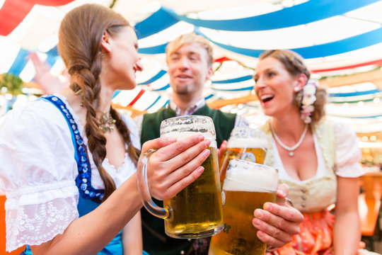 Drei Freunde im Bierzelt auf bayerischem Volksfest stoßen mit Bier an