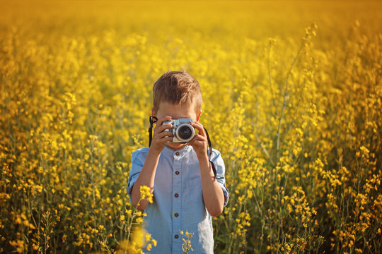 Portrait of little boy photographer with camera on sunset yellow field background