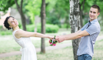 Portrait of happy beautiful young couple female bride with small wedding flowers roses bouquet and male bridegroom holding hands, smiling and spinning in summer park