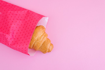 Fresh croissant in pink paper wrap on pink background