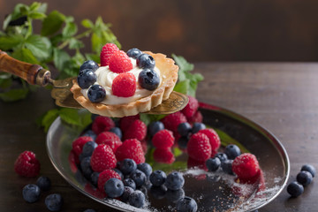  Dessert tarts with raspberries and blueberries on a wooden table.