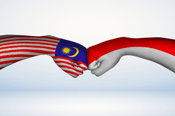 Fist bump of Malaysian and Indonesian flags.
Two hands with painted flags of Malaysia and...