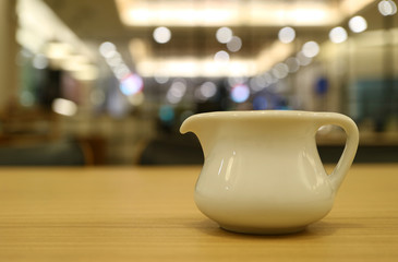 Closed up a white ceramic pitcher on cafe's wooden table with bokeh interior lighting in the background 
