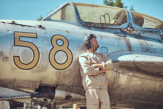 Pilot in uniform and flying helmet standing near an old war fighter-interceptor in an open-air museum.