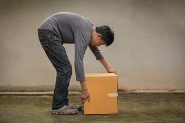  young man bent down, raised cardboard box in an ergonomic posture. - obrazy, fototapety, plakaty