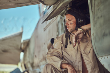 Portrait of a mechanic in uniform and flying near, standing under an old bomber airplane in the...