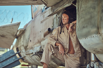 Portrait of a mechanic in uniform and flying near, standing under an old bomber airplane in the open air museum.