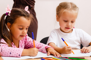 Two teachers in class with their young students with a beautiful young woman helping two small girls at a desk