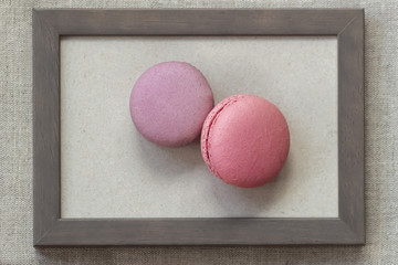 Fresch macaroons of pink and violet colors in wooden frame on wall, unusual abstract sweet art