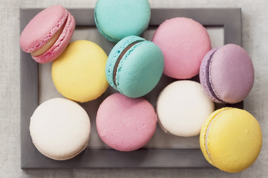 Fresh natural colorful macarons of different tastes in wooden frame, unusual abstract sweet art, gourmet picture