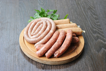 Assorted raw sausages on a round wooden board. Sausages of pork, beef and chicken. Dark background. Close-up.