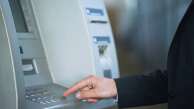 Male hands entering pin code on ATM keyboard, withdrawing money from account