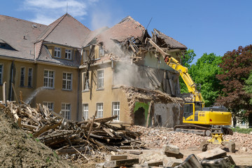 Fototapeta na wymiar Big yellow excavator breaks down old house at summer