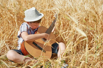child with guitar is in the yellow wheat field, bright sun, summer landscape