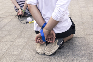 Two people with their hands tied behind their backs sit on their knees in the city square, a social...
