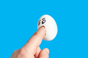 Fototapeta na wymiar Angry white chicken egg with eyes biting finger
