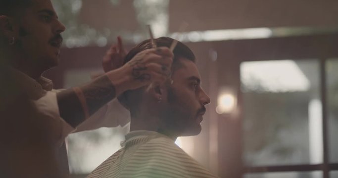 Young stylish barber with tattoos cutting and styling man's hair