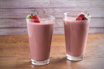 Two glasses of chocolate strawberry milkshake or cocktail on wooden table.  Strawberry chocolate smoothie with berries. Healthy drinks. horizontal