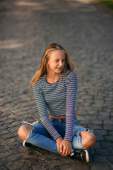 A teenage girl in jeans and a blouse and sits in the middle of the street