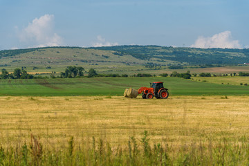 Tractor lifting hay bale on barrow.