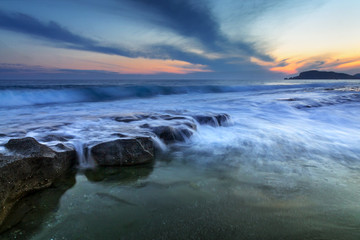 Waves hitting the rocks at sandy Alanya beaches during sunset