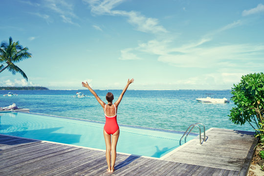 Feel freedom! Young woman in red swimsuit enjoying the view near swimming pool on tropical beach.