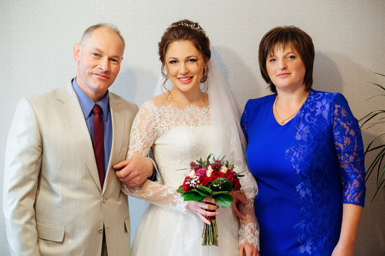 Happy Parents And The Daughter Who Gets Married, Dressed In A Wedding Dress And A Bouquet In Her Hand