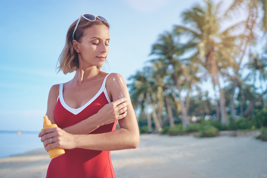 UV protection and suntan. Young pretty woman holding bottle with sunscreen lotion on tropical beach.
