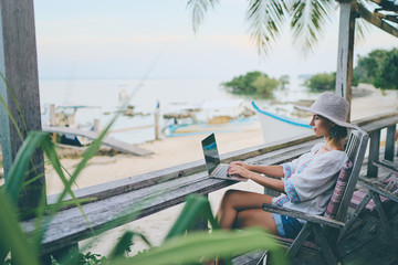 Technology and travel. Working outdoors. Freelance concept. Pretty young woman using laptop in cafe on tropical beach.