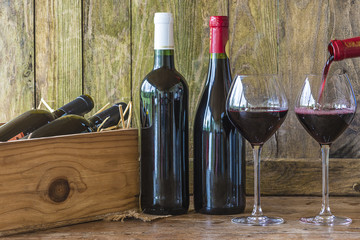 Bottles of red wine and wineglasses on rustic background