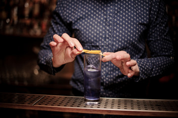 Bartender decorating a glass of violet cocktail with an orange pill