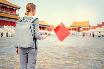 Enjoying vacation in China. Traveling young woman with national chinese flag in Forbidden City, Beijing.