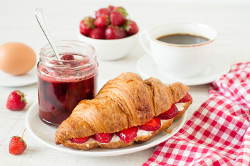 Breakfast with coffee, croissant and strawberry jam on a table